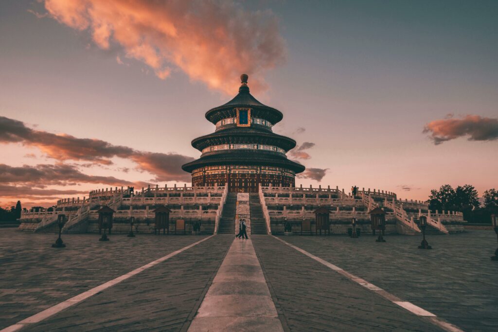 Deux personnes marchant au coucher du soleil devant le Temple du ciel de Pékin.