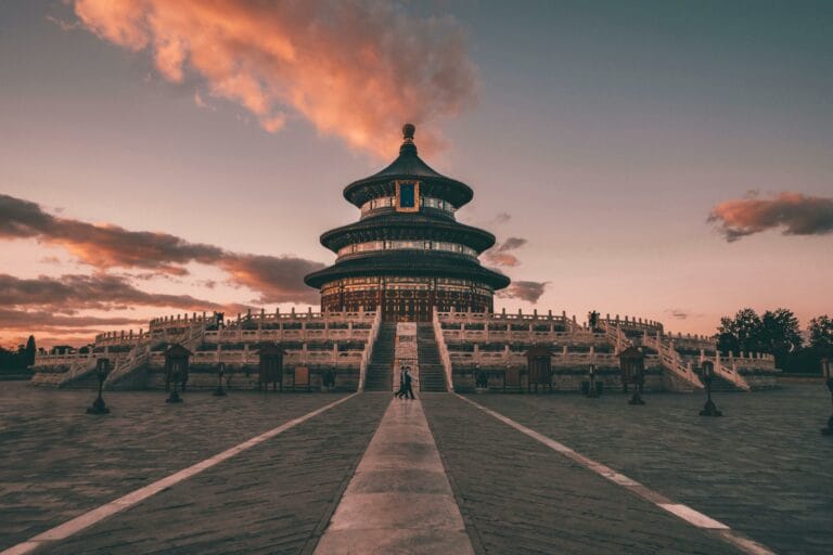 Deux personnes marchant au coucher du soleil devant le Temple du ciel de Pékin.