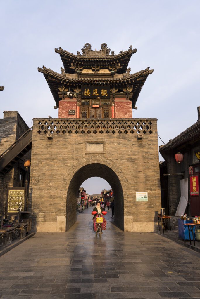Une femme qui fait du vélo et qui vient juste de passer sous la tour de guet Fengshui à Pingyao, province de Shanxi, Chine.